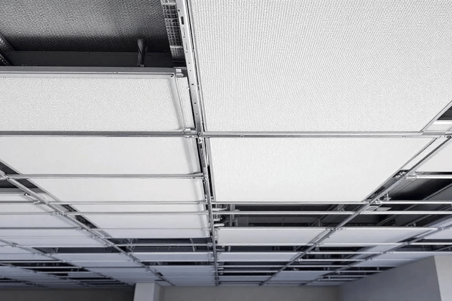 The image features a close-up view of a drop ceiling installation showcasing the metal grid system and acoustic tiles, highlighting the suspended ceiling's structure. The image features a close-up view of a drop ceiling installation showcasing the metal grid system and acoustic tiles, highlighting the suspended ceiling's structure. This installation allows for easy access to overhead space and is designed for noise reduction, making it ideal for spaces like basements and commercial areas.