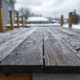 The image shows pressure-treated lumber deck boards being installed under cold weather conditions, with snow accumulation on the ground. The scene highlights the challenges of deck design in harsh winter climates, emphasizing the importance of proper spacing and load requirements to ensure structural integrity.